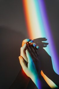 Imagem de duas mãos sobre a luz de um arco-íris.