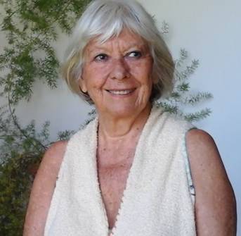 Retrato de Lygia Bojunga, de cabelo branco e blusa clara, diante de plantas.